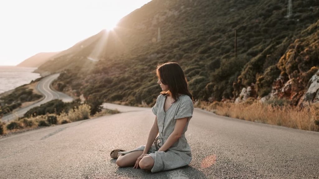 A woman sitting on a coastal road in Antalya during sunset, offering a serene landscape view.