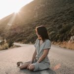 A woman sitting on a coastal road in Antalya during sunset, offering a serene landscape view.