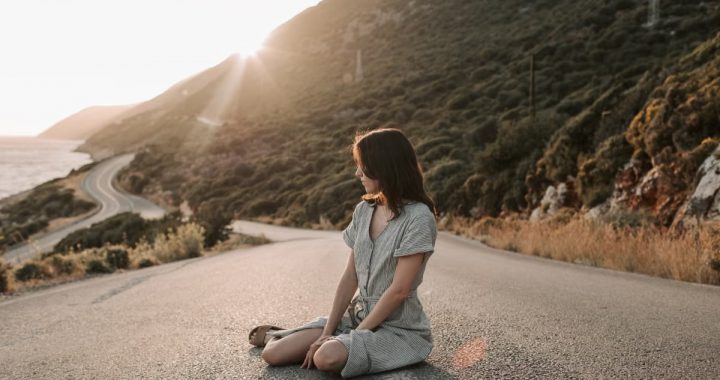 A woman sitting on a coastal road in Antalya during sunset, offering a serene landscape view.