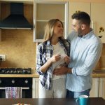 Attractive girl shows pregnancy test result to her boyfriend and surpise him at the kitchen . Loving couple embrace and kissing at home because of good news