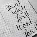 Close-up of motivational calligraphy on grid paper, inspiring message for productivity.